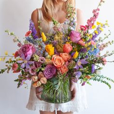 a woman holding a vase filled with lots of flowers