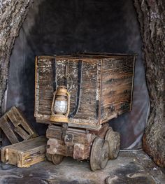 an old wooden cart with a lantern in it sitting next to some wood crates under a tree