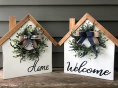 two wooden houses with wreaths and welcome home signs on the front, one painted white