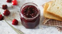 a jar filled with jam next to slices of bread and cherries on a table