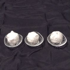 three silver plates with whipped cream on them sitting on a black cloth covered tablecloth