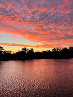 the sky is pink and orange as it sits over water with trees in the background