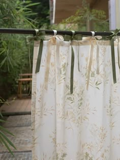 the curtains are hanging outside in front of some trees and bushes with green ribbons on them