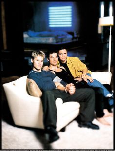 three people sitting on a white couch in front of a flat screen tv set with one person holding his arm around the other