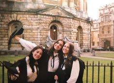 three young women posing for a photo in front of a building with a gate and iron fence