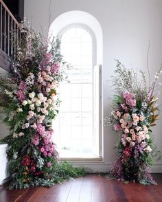 two tall floral arrangements in front of a window with an arched window sill behind them