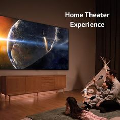 a man and child sitting on the floor in front of a large screen tv with an image of space