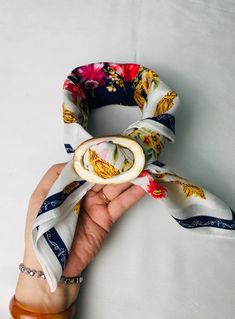 a hand holding a white and blue flowered scarf with an open ring on it