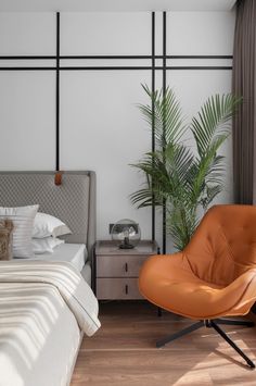 an orange chair sitting in front of a bed next to a tall plant on top of a wooden floor