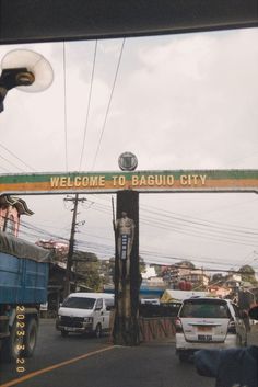 the welcome sign to baquo city is posted above a busy street