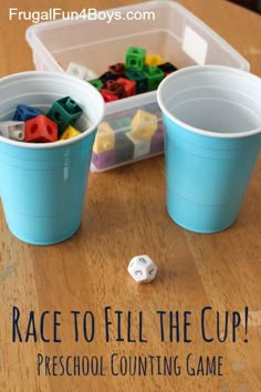 two plastic cups filled with legos sitting on top of a wooden table next to a dice