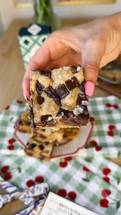 a person holding up a piece of chocolate chip cookie bar on top of a plate