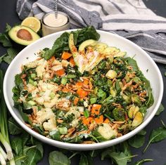 a white bowl filled with salad next to an avocado and some other vegetables