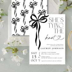 a white and black wedding card with a bow on it, next to some flowers