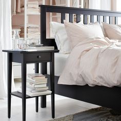 a bed with white sheets and pillows next to a night stand filled with books on top of it