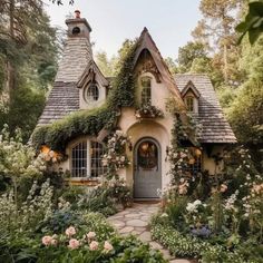 a small house with lots of flowers and greenery on the front door, surrounded by trees