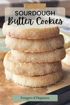 a stack of sugary cookies sitting on top of a wooden cutting board with the words sourdough butter cookies