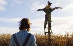 a woman looking at a scarecrow in a cornfield with the sun shining on her