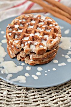 two waffles on a blue plate with cinnamon sticks in the background and white icing