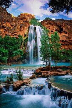 the waterfall is surrounded by green trees and rocks, with blue water running down it