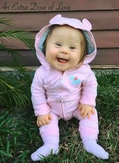 a baby sitting in the grass wearing a pink outfit