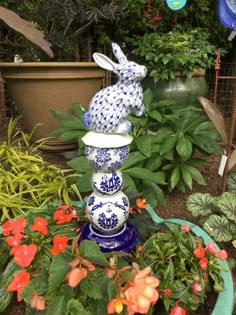 a blue and white rabbit statue sitting on top of a flower pot filled with flowers