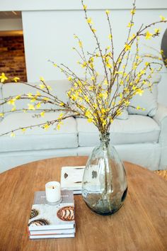 a vase with yellow flowers sitting on top of a wooden table next to a couch