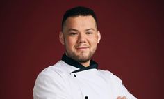 a man with his arms crossed wearing a chef's coat and black collared shirt