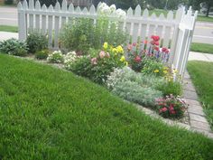 a white picket fence surrounded by flowers and grass