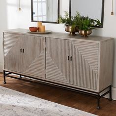 a sideboard with two mirrors and plants on top