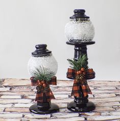 two snow globes decorated with pine cones and bows are sitting on top of a table