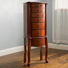 a wooden jewelry cabinet sitting on top of a hard wood floor next to a window