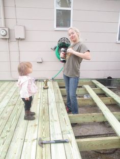 a woman is holding a hose and standing next to a toddler on a wooden deck