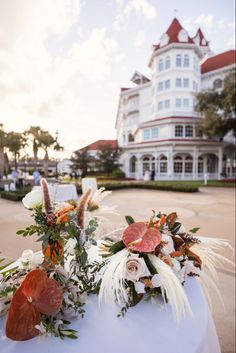 flowers and foliage sit on top of a white table in front of a large building