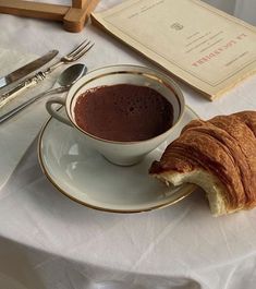 a croissant on a plate next to a cup of chocolate