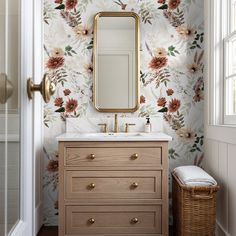 a bathroom with floral wallpaper and a gold framed mirror above the sink, along with a wicker basket on the floor