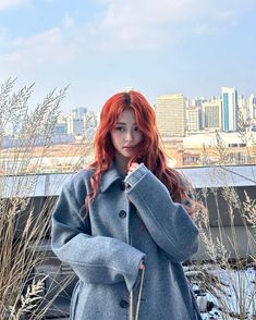 a woman with red hair is standing in front of tall grass and looking at the camera