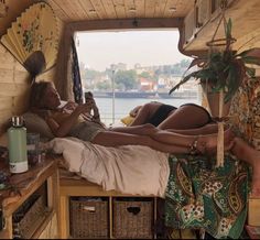 two women laying on a bed in the back of a small van with an open window