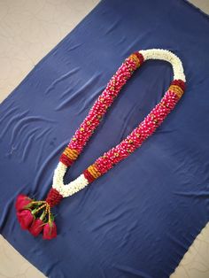 a flower decorated necklace laying on top of a blue sheet with red and white beads