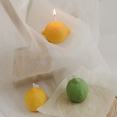 two lemons and an orange on a white cloth with a candle in the background