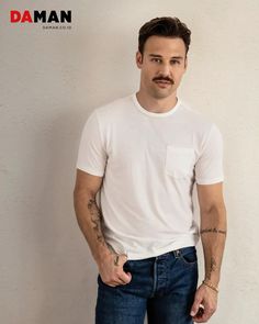 a man standing in front of a white wall wearing jeans and a t - shirt