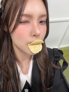 a woman with long brown hair wearing a black jacket and eating a piece of food