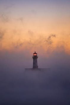 a light house in the middle of foggy water at sunset with clouds around it