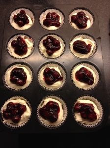 twelve cupcakes with white frosting and cherries in the middle, ready to be baked