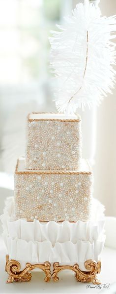 a three tiered cake with white frosting and pearls on the top is sitting on a gold stand