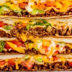 three tacos stacked on top of each other with cheese, lettuce and tomatoes