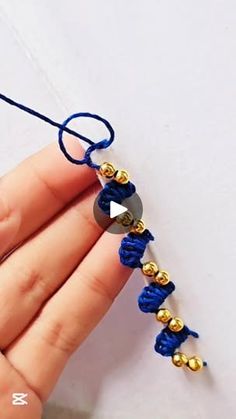 someone is making a bracelet with blue thread and gold beads on the end, while holding it in their hand