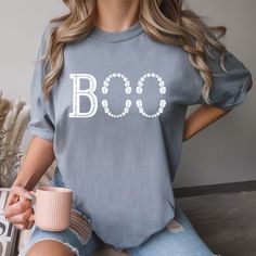 a woman sitting on a couch holding a cup and wearing a t - shirt that says boo