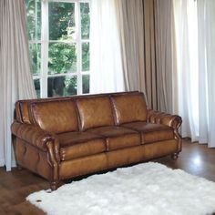 a brown leather couch sitting in front of a window next to a white rug on top of a hard wood floor