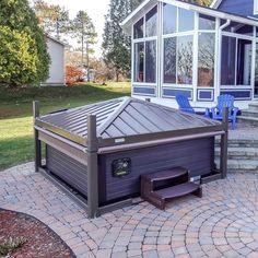 an outdoor hot tub sitting on top of a brick patio next to a blue house